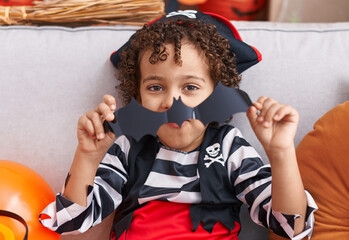 Adorable hispanic boy having halloween party holding bat paper at home