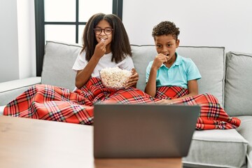 Brother and sister watching movie sitting on sofa at home