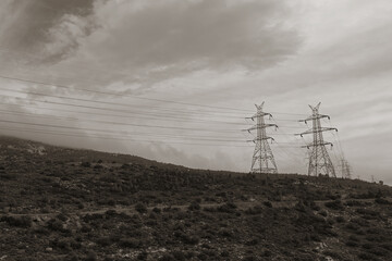 pylons overhead power lines on mountain and cloudy sky