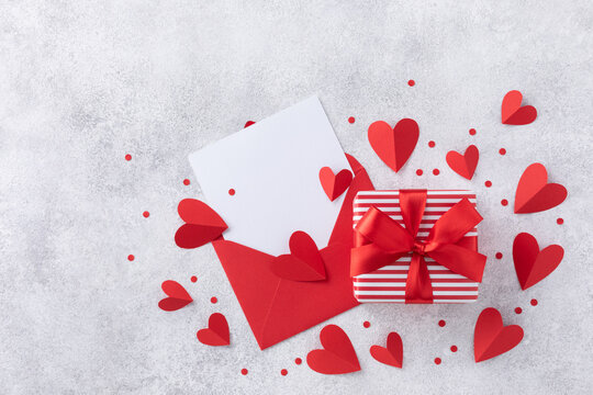 Valentine day holiday background with envelope, paper card, gift box and various red hearts for love romantic message. Romantic composition in flat lay style.. - Powered by Adobe