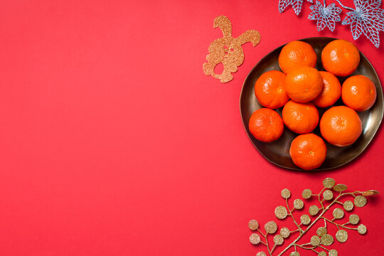Chinese or lunar new year flat lay with plate of mandarins, paper rabbits as symbol of 2023 and flowers on red