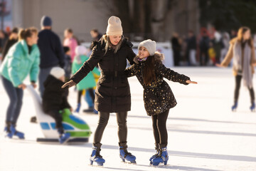 Action shot of beautiful woman teaching her daughter how to ice skate