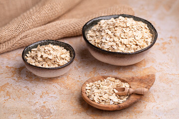 Oat flakes, cereal in handmade ceramic bowls and in a wooden bowl on burlap on a beige stone table, cereal scoop