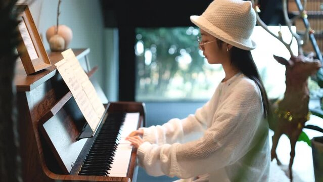 Asian girl playing piano at home, hobbies to enhance concentration and relaxation.