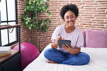African american woman using touchpad sitting on bed at bedroom