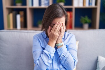 Middle age hispanic woman sitting on the sofa at home with sad expression covering face with hands while crying. depression concept.