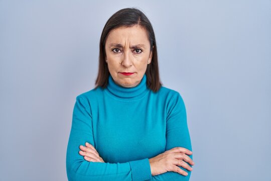 Middle age hispanic woman standing over isolated background skeptic and nervous, disapproving expression on face with crossed arms. negative person.