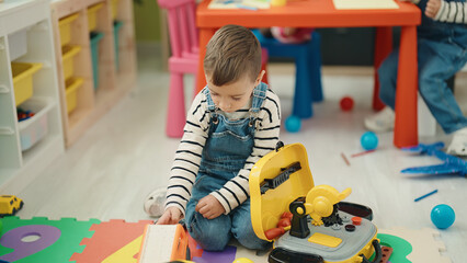 Adorable caucasian boy playing with toys sitting on floor at kindergarten