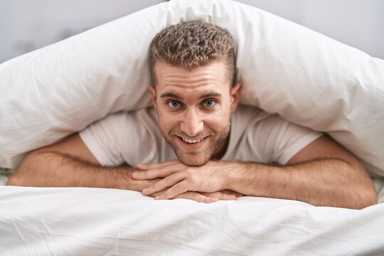 Young caucasian man lying on bed covering with bedsheet at bedroom