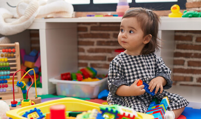 Adorable chinese girl playing with construction blocks sitting on floor at kindergarten