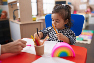 Adorable chinese girl preschool student sitting on table drawing on paper at kindergarten