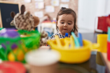 Adorable chinese girl playing with play kitchen holding fork toy at kindergarten