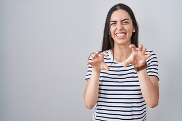 Young brunette woman wearing striped t shirt smiling funny doing claw gesture as cat, aggressive...