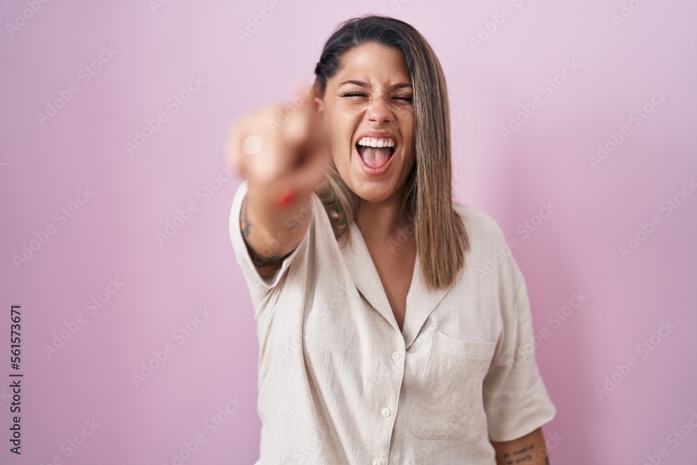 Poster blonde woman standing over pink background pointing displeased and frustrated to the camera, angry a