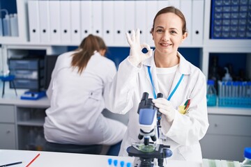 Blonde woman working on cruelty free laboratory doing ok sign with fingers, smiling friendly gesturing excellent symbol
