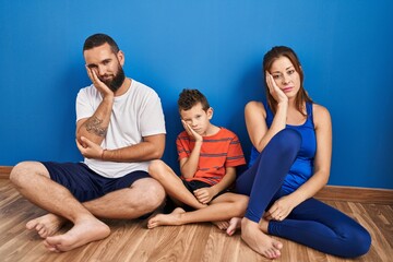 Family of three sitting on the floor at home thinking looking tired and bored with depression...