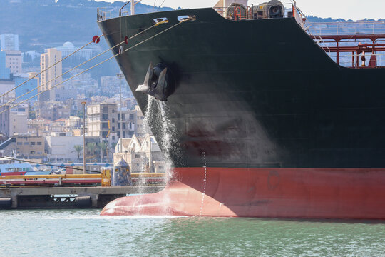 Large anchored cargo ship discharging ballast water out from Anchor's hub.