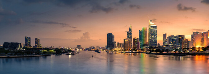 Naklejka premium Aerial sunset view of Bitexco Tower, buildings, roads, Bason bridge and Saigon river in Ho Chi Minh city, container cargo ship on Saigon river. Travel concept.