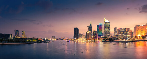 Fototapeta premium Aerial sunset view of Bitexco Tower, buildings, roads, Bason bridge and Saigon river in Ho Chi Minh city, container cargo ship on Saigon river. Travel concept.