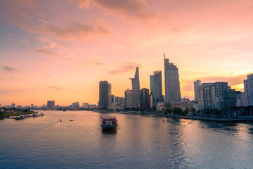 Fototapeta premium Aerial sunset view of Bitexco Tower, buildings, roads, Bason bridge and Saigon river in Ho Chi Minh city, container cargo ship on Saigon river. Travel concept.