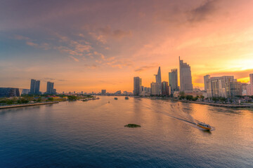 Fototapeta premium Aerial sunset view of Bitexco Tower, buildings, roads, Bason bridge and Saigon river in Ho Chi Minh city, container cargo ship on Saigon river. Travel concept.