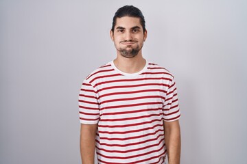 Hispanic man with long hair standing over isolated background puffing cheeks with funny face. mouth...