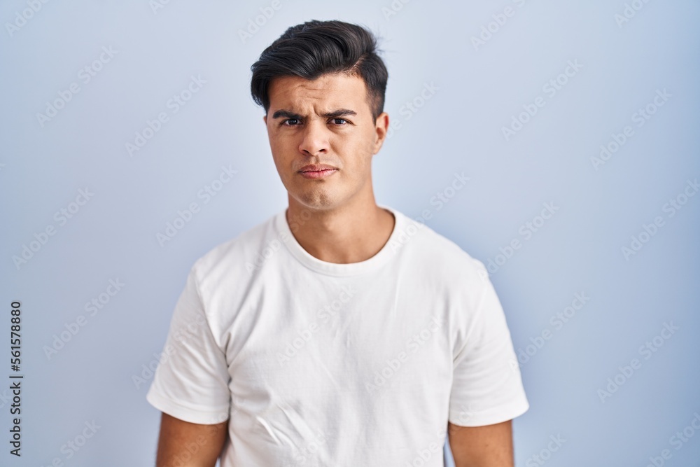 Sticker Hispanic man standing over blue background skeptic and nervous, frowning upset because of problem. negative person.