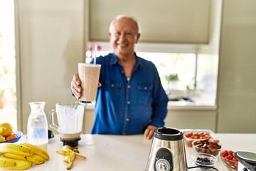Senior man smiling confident holding glass of smoothie at kitchen