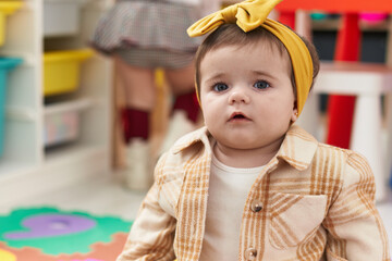 Adorable blonde toddler sitting on floor with serious expression at kindergarten
