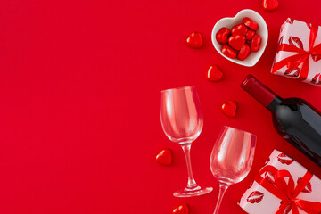 Valentines Day mood concept. Top view photo of red gift boxes, wine bottle with glasses, heart shaped saucers with candies and lollipops, sprinkles on red background. Flat lay with copy space.
