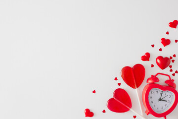 St Valentine's Day concept. Flat lay photo of red heart shaped lollipops, alarm clock and hearts sprinkles on white background with copy space. Minimal Valentines card idea.
