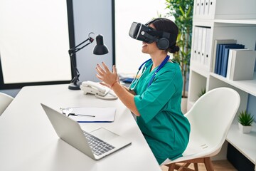 Young beautiful hispanic woman doctor using virtual reality glasses at clinic