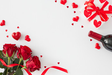 Love or Valentines concept. Flat lay composition made of red roses with ribbon, wine bottle, gift box, red hearts on white background with copy space in the middle. Holiday card idea.
