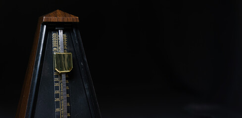 Mechanical metronome on a dark plain background. Panorama photo, background for banner on website