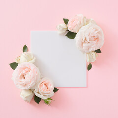 Top view of spring flowers with green leaves and white frame on pastel pink background. Minimal flat lay nature background. Valentines or woman's day concept.