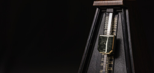 Mechanical metronome on a dark plain background. Panorama photo, background for banner on website