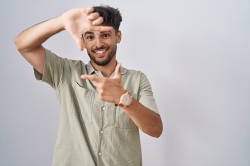 Fototapeta premium Arab man with beard standing over white background smiling making frame with hands and fingers with happy face. creativity and photography concept.