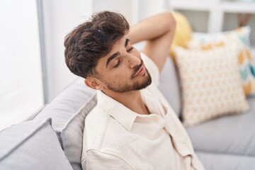 Young arab man relaxed with hand on head sitting on sofa at home