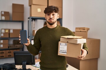 Arab man with beard working at small business ecommerce holding delivery packages puffing cheeks...