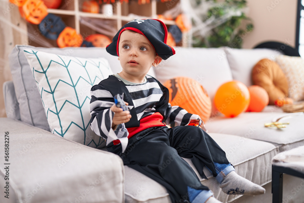 Sticker Adorable hispanic boy having halloween party holding pumpkin basket and car toy at home