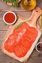 Chorizo sausage and salami, thin cut. Spanish salami on the wood background with spices, paprika, rosemary and olives. Spicy food. Antipasto and appetizer meat. 