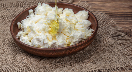A large bowl with homemade cottage cheese and honey on a wooden table.