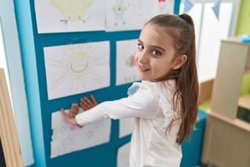 Fototapeta na wymiar Adorable hispanic girl preschool student hanging draw on wall at kindergarten