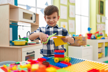 Adorable hispanic boy student smiling confident cutting paper at kindergarten