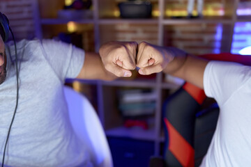 Two hispanic men streamers bumping fists at gaming room