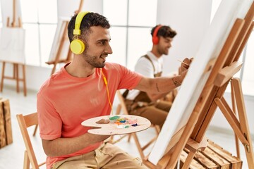 Two hispanic men couple listening to music and drawing at art studio