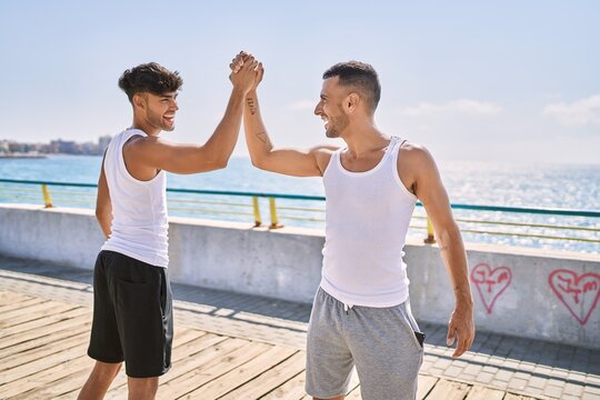 Two hispanic men couple smiling confident high five with hands raised up at seaside