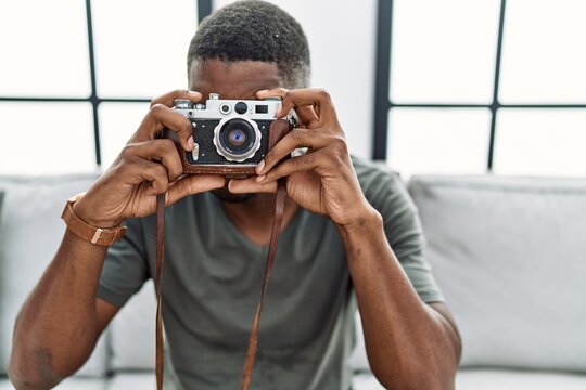 Young african american man smiling confident using vintage camera at home