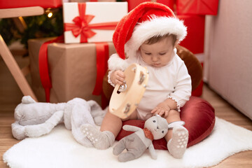 Adorable toddler holding tambourin sitting on floor by christmas gift at home