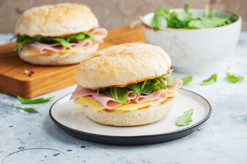 Two homemade sandwiches with ham, cheese and arugula on a concrete table.